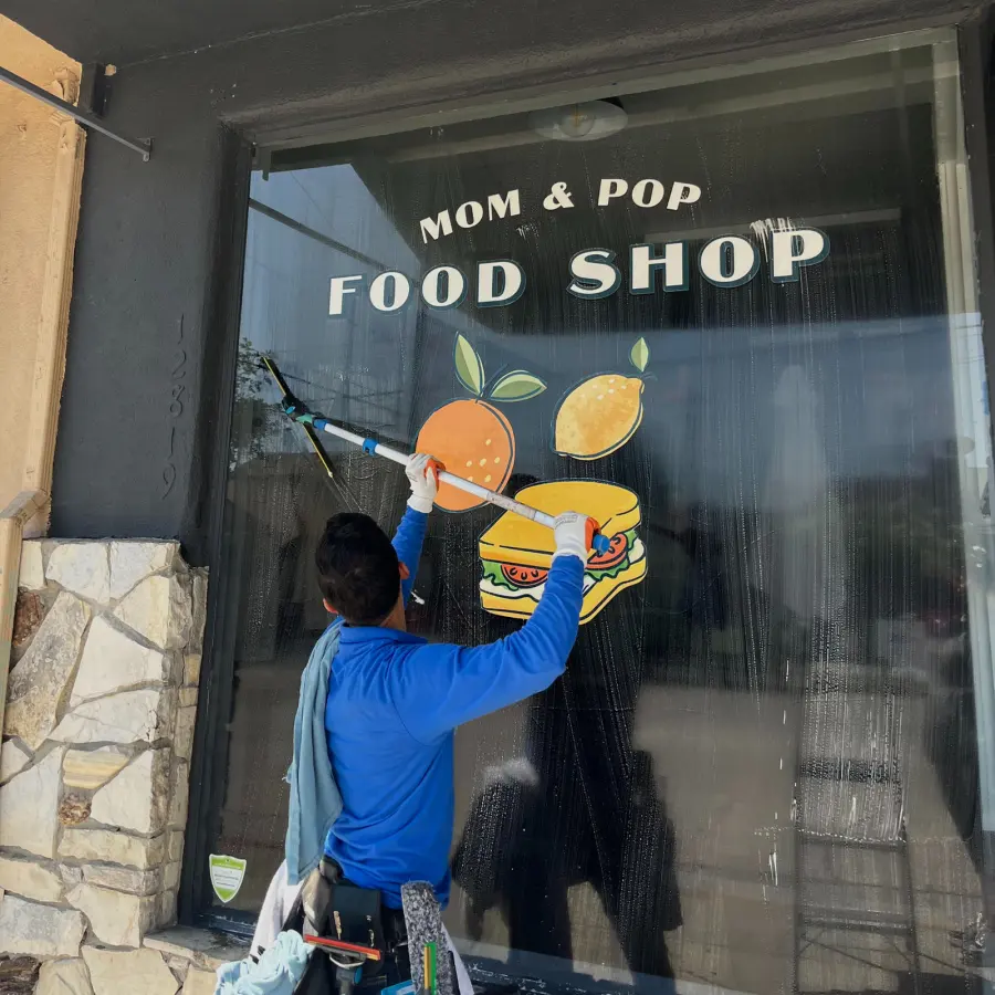 DCS technician cleaning the window of a local storefront with a squeegee on a pole