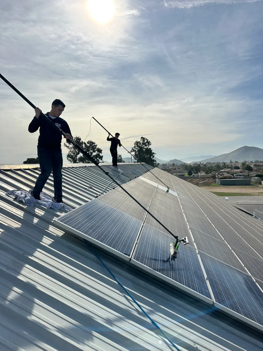 DCS technician on a rooftop cleaning a solar array with a water-fed pole