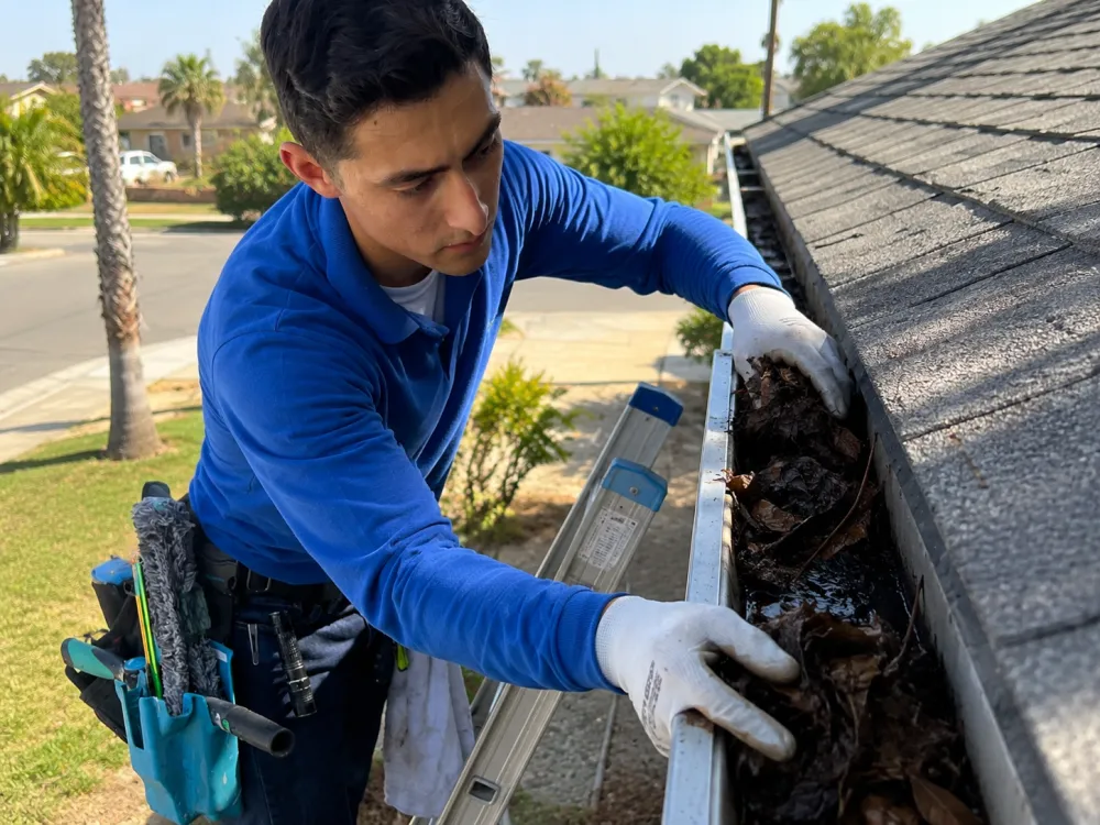 Technician clearing debris from a residential rain gutter
