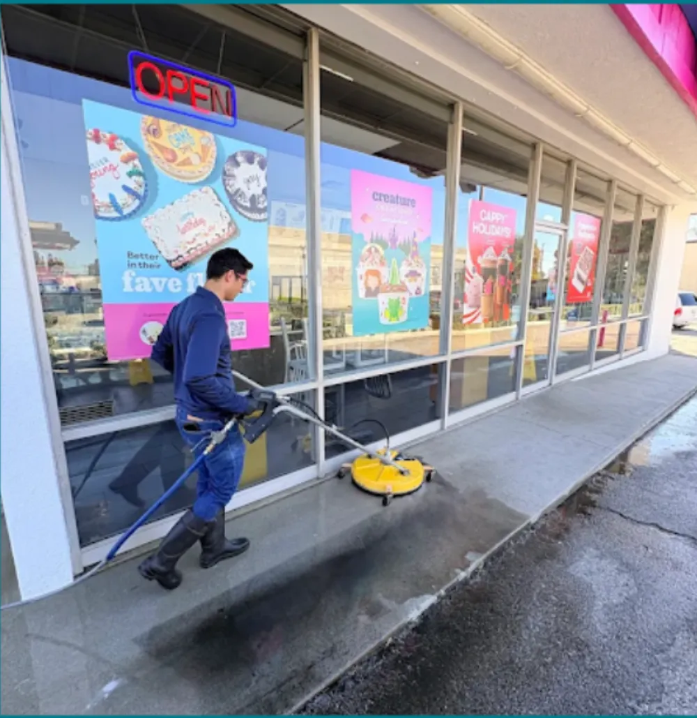 DCS technician pressure washing a commercial storefront sidewalk with a surface cleaner