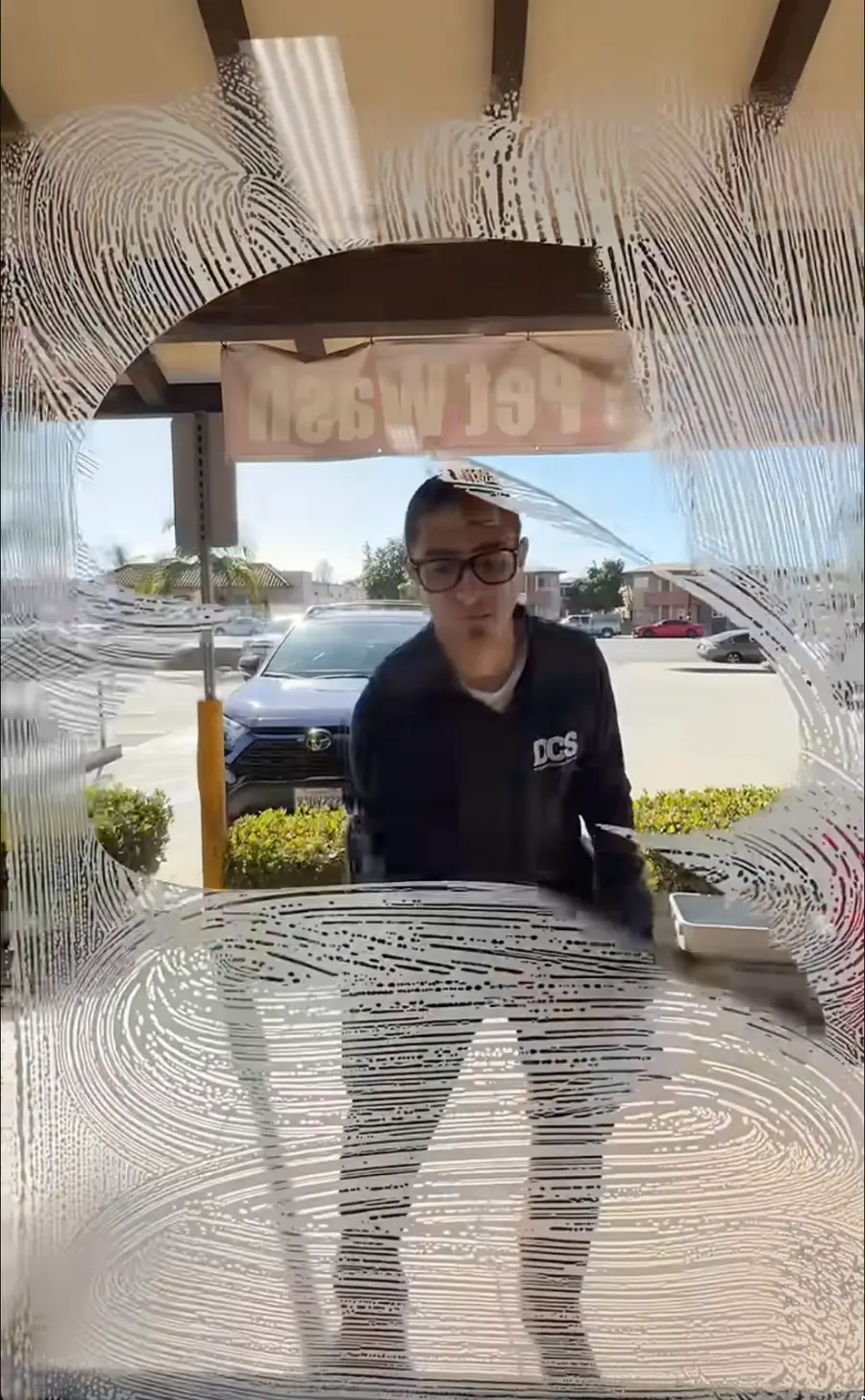 Dynamic Cleaning Services technician in a branded polo cleaning storefront glass at a local business